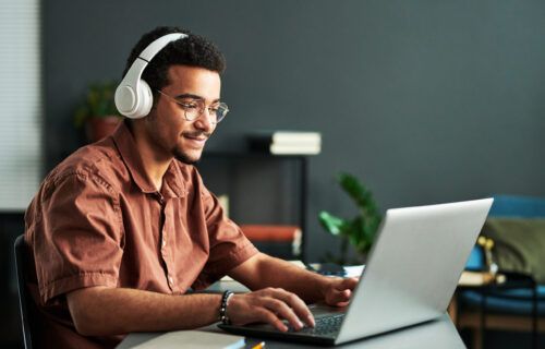 young-smiling-man-in-headphones-typing-on-laptop-keyboard
